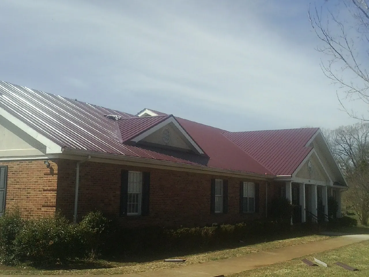 Red metal roof with gabled entries on a long brick building, from a Hail Damage Roof Repair job in Skull Valley