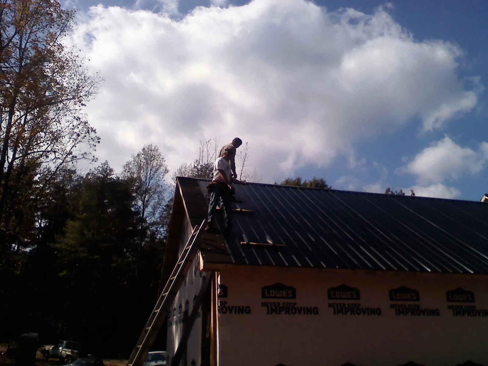 Roofer fastening dark metal panels high against a cloudy sky, from a Roof Inspection job in Skull Valley